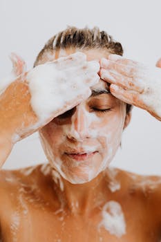 Close-up of a woman calmly washing her face with foam cleanser, focusing on skincare and relaxation.