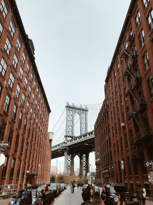 Free Classic view of Manhattan Bridge framed by red brick buildings on a busy Brooklyn street. Stock Photo