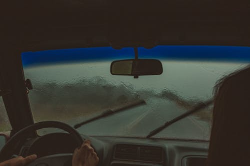 Crop unrecognizable travelers sitting in automobile with wet windshield and wipers in rainy weather