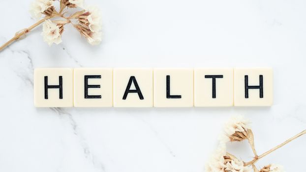 Creative arrangement of scrabble tiles spelling 'Health' with white flowers on a marble surface.
