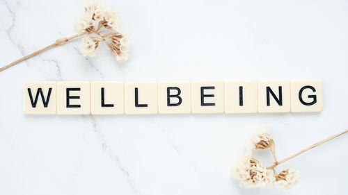 Free Scrabble tiles spell 'Wellbeing' amid delicate white flowers on a marble background. Stock Photo