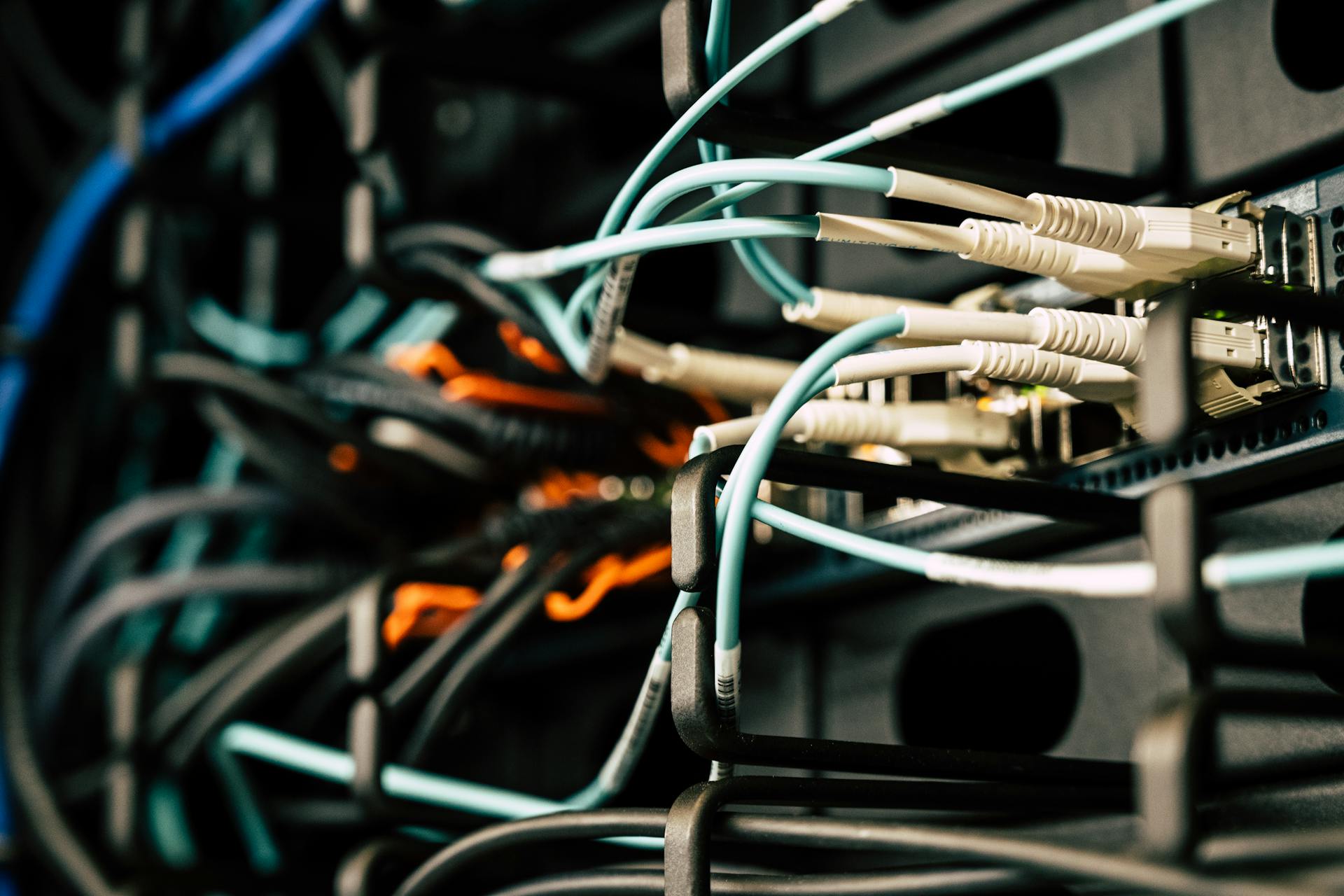 Various tangled wires connected to system near black metal cases in server room