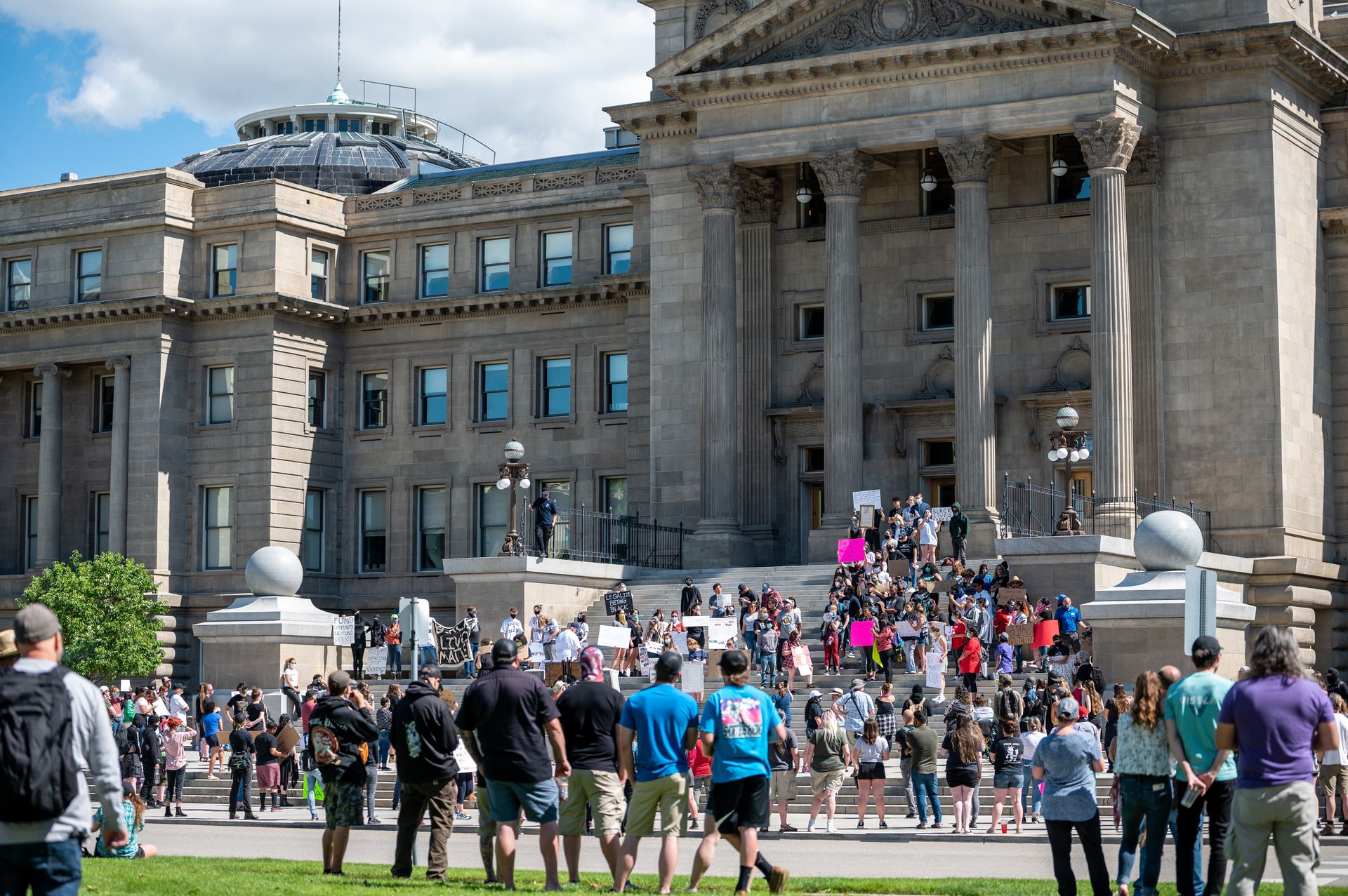 A diverse group of individuals gather for a peaceful protest at a historic government building on a sunny day.