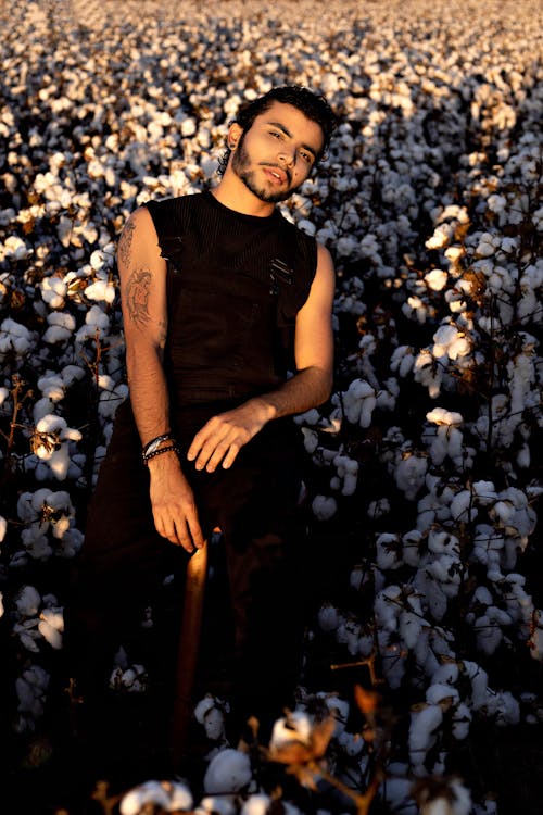 Bearded ethnic male posing and squinting in blooming plantation in rays of bright sun