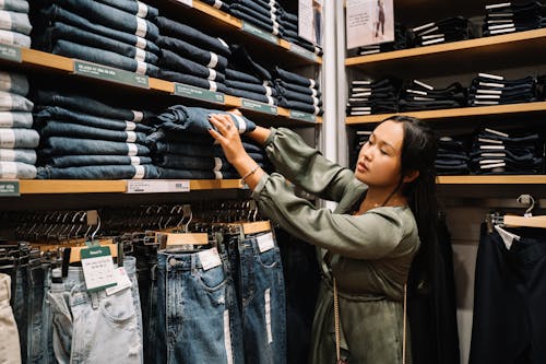 Woman Looking at the Jeans on a Wooden Shelf