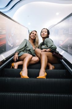 两名时尚女性坐在现代建筑的自动扶梯上，显得自信又时髦
