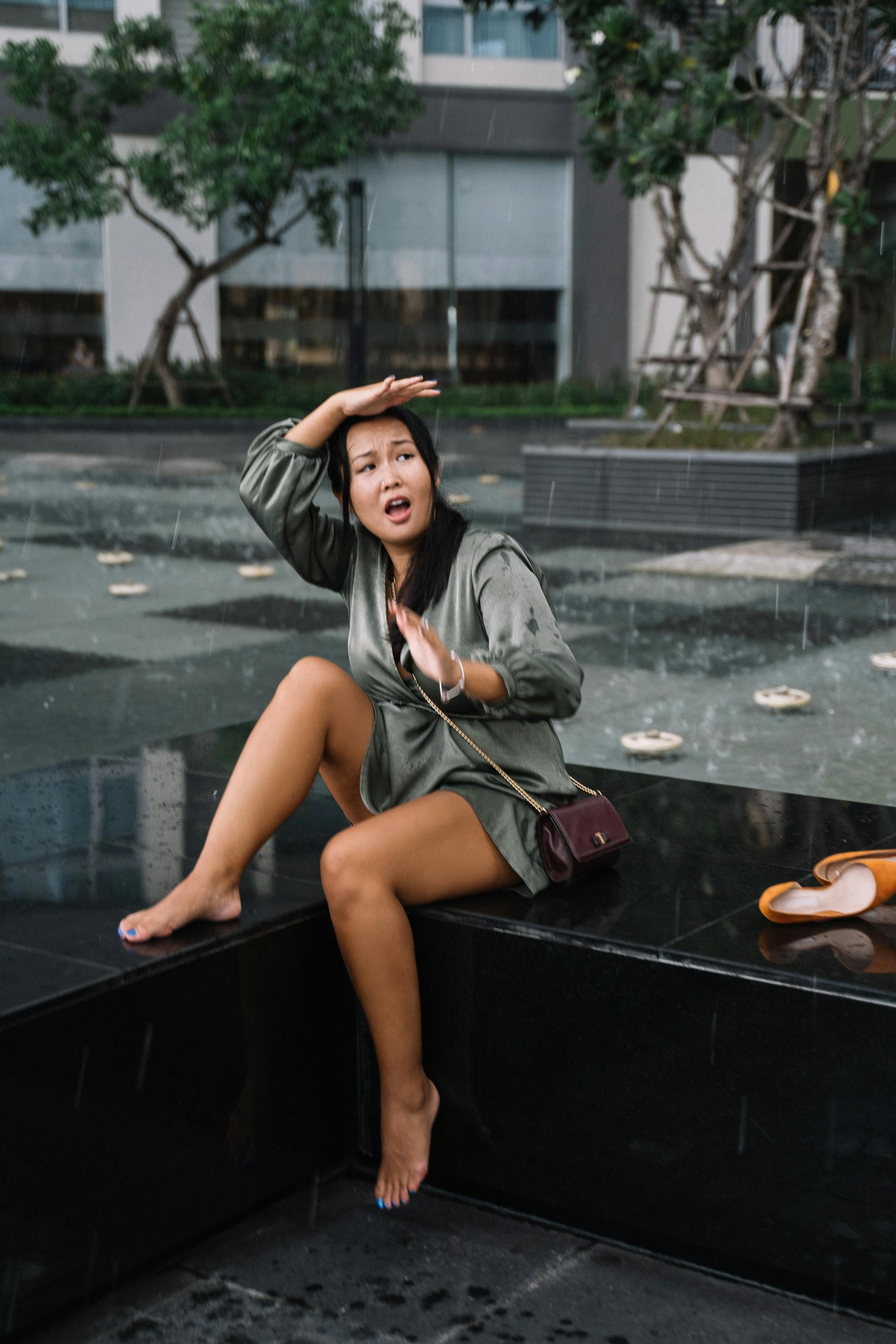 一名年轻女子顽皮地坐在城市喷泉附近