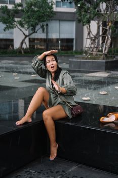 一名年轻女子顽皮地坐在城市喷泉附近