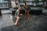 两名女子在城市广场上快乐地拥抱突然的阵雨，欢笑着，玩得很开心