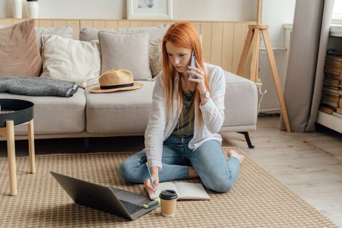 Free A woman sitting on the floor using a laptop and phone in a modern home office environment. Stock Photo