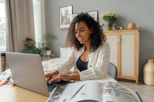 Free An African American woman smiling while using a laptop at a cozy home workspace. Stock Photo