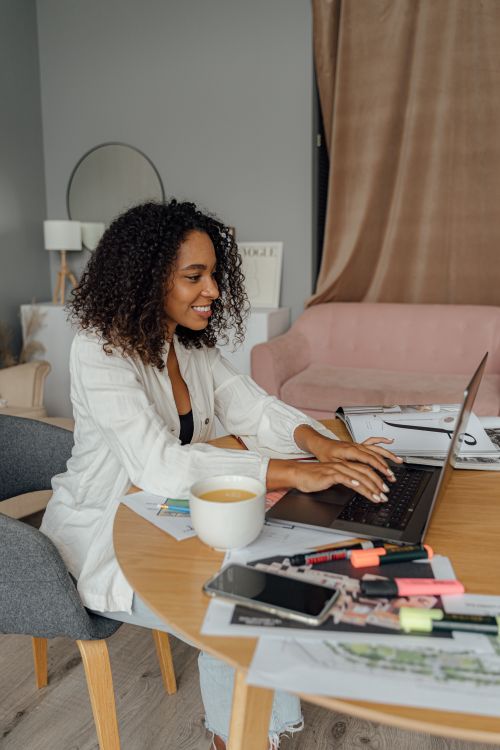 Free Smiling African American woman working on a laptop at home in a modern setting, enjoying her workspace. Stock Photo