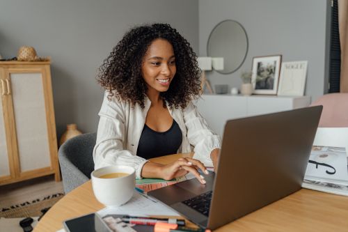 Free A woman sits at a round table, working on a laptop with a coffee cup nearby in a cozy home office setting. Stock Photo