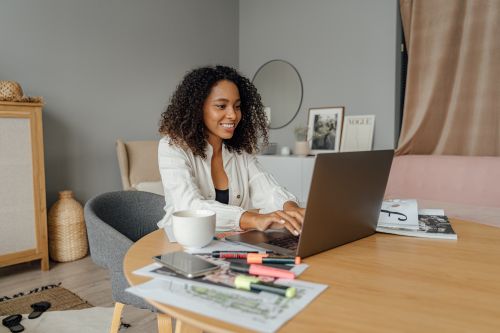 Free A happy woman working on a laptop in a cozy home office, enjoying freelance work. Stock Photo