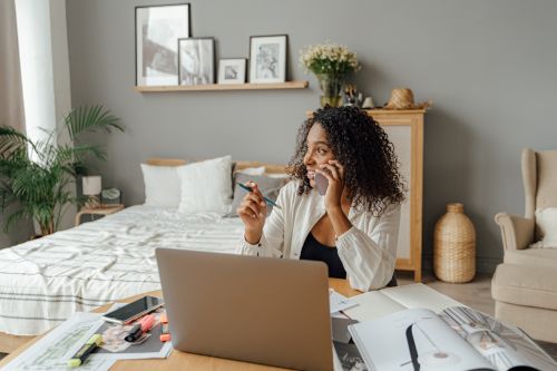 Free A woman in a home office multitasking with a laptop and phone call, surrounded by documents. Stock Photo