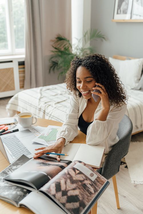 Free Young woman juggling phone call, magazine browsing, and work on laptop at home office. Stock Photo