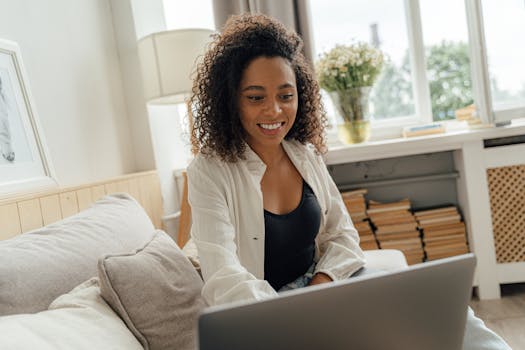 Smiling woman enjoying her time indoors, sitting on a sofa and using a laptop.