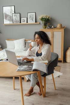 Black woman working remotely in cozy home office, sipping coffee.