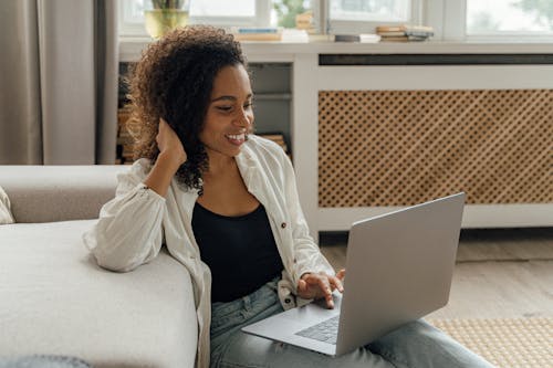 Woman in White Long Sleeve Using a Laptop while Sitting on the Floor