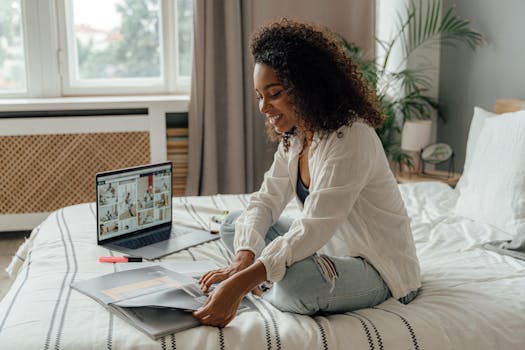 Smiling woman working on bed with laptop and papers, embracing remote work lifestyle.