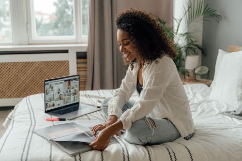 Free Smiling woman working on bed with laptop and papers, embracing remote work lifestyle. Stock Photo
