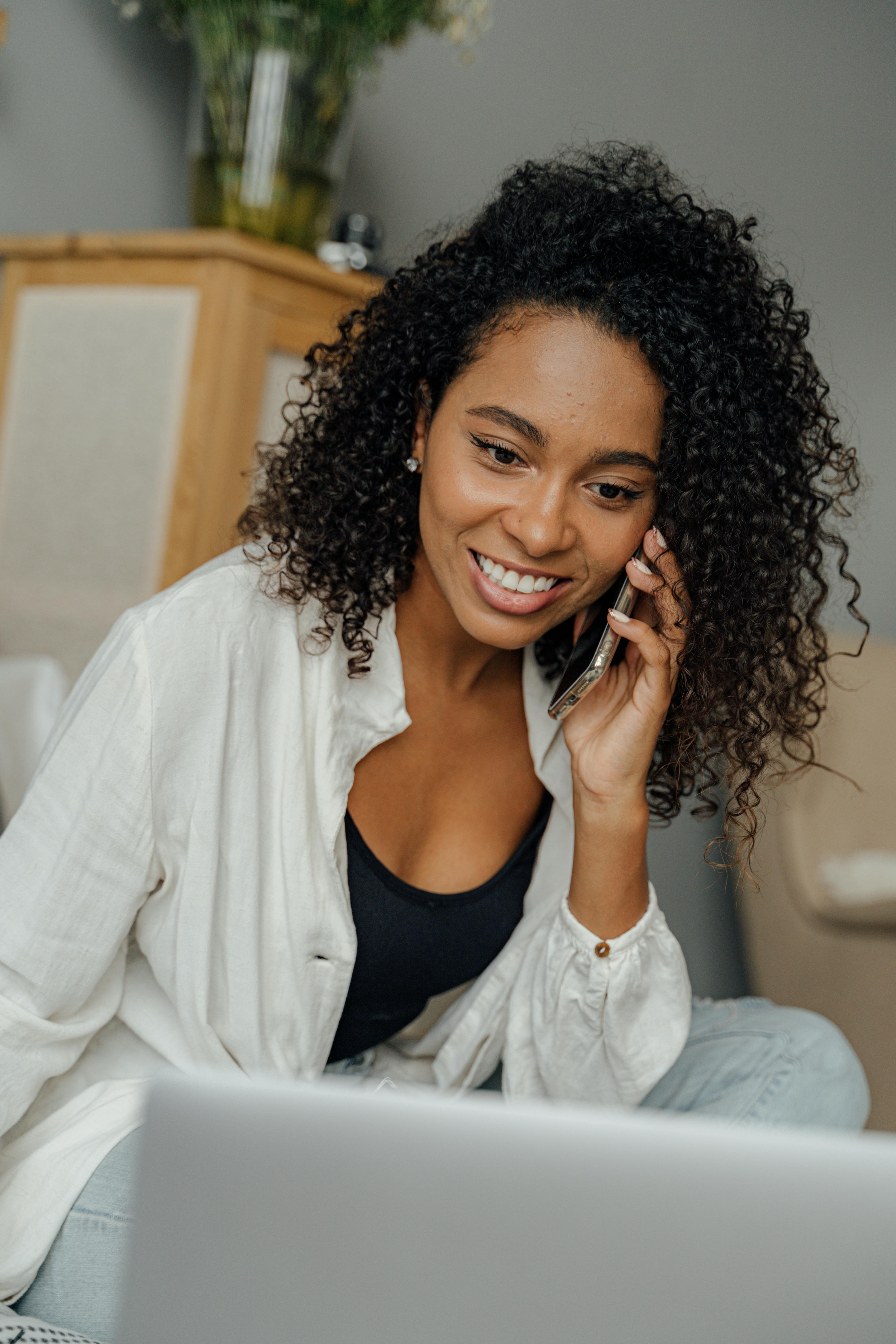 woman in white long sleeve using a laptop while having a phone call