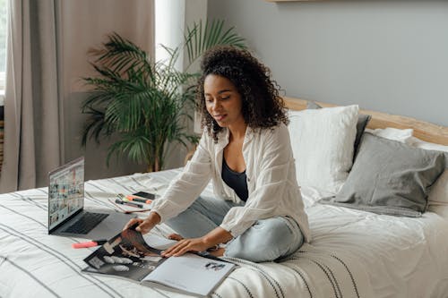 Woman in White Long Sleeve Using a Laptop while Sitting on the Bed