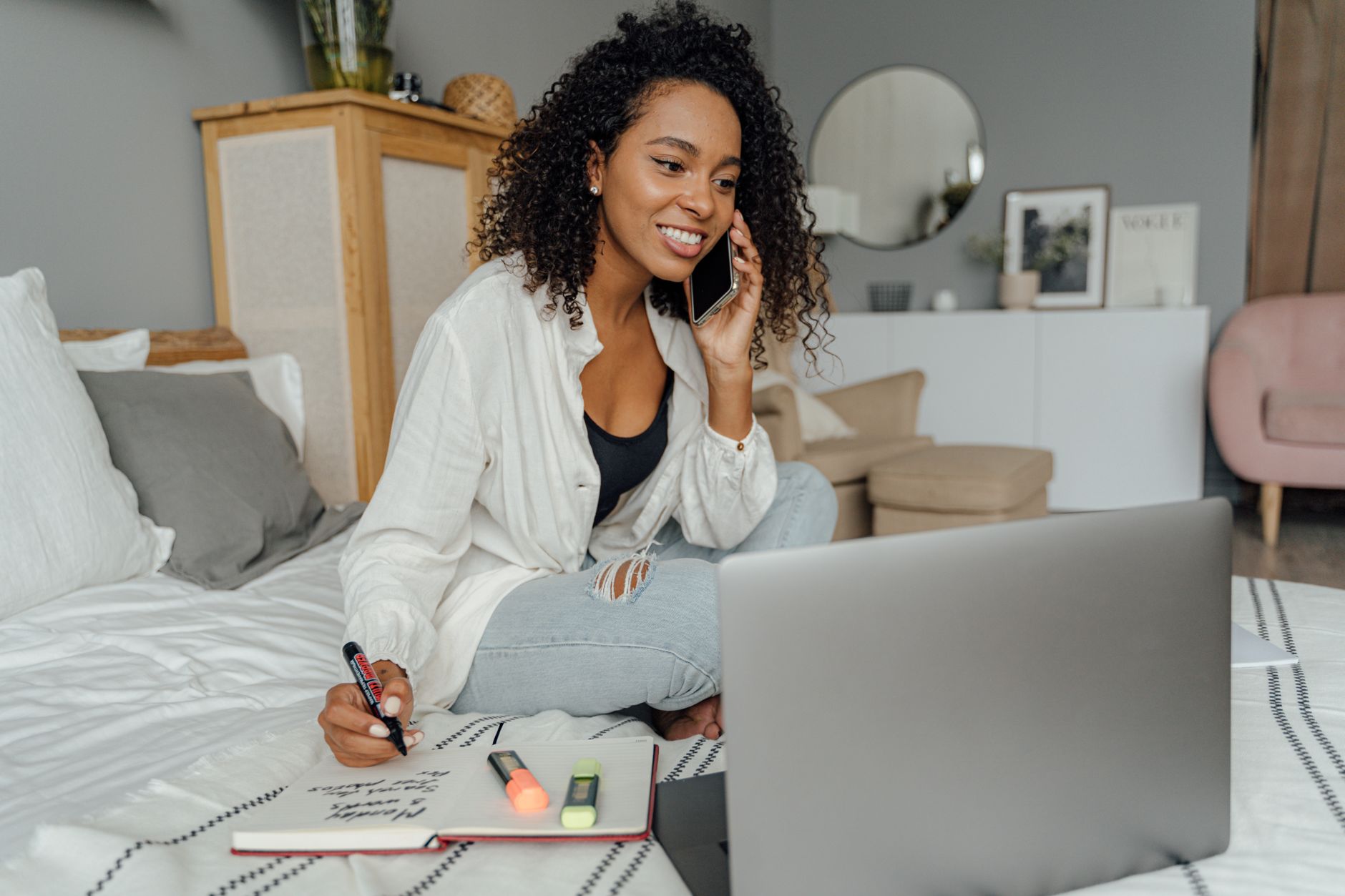 How to Troubleshoot Video Calls Lagging While Multitasking Smiling woman multitasks during a remote work call, seated with laptop and notepad.