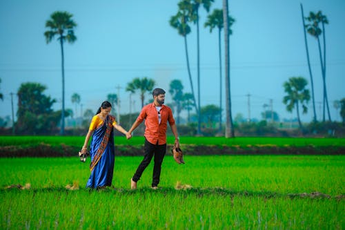 A Couple Holding Hands While Walking on a Field