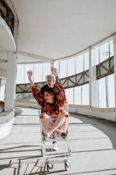 两个成年人在停车场里骑着购物车晒太阳