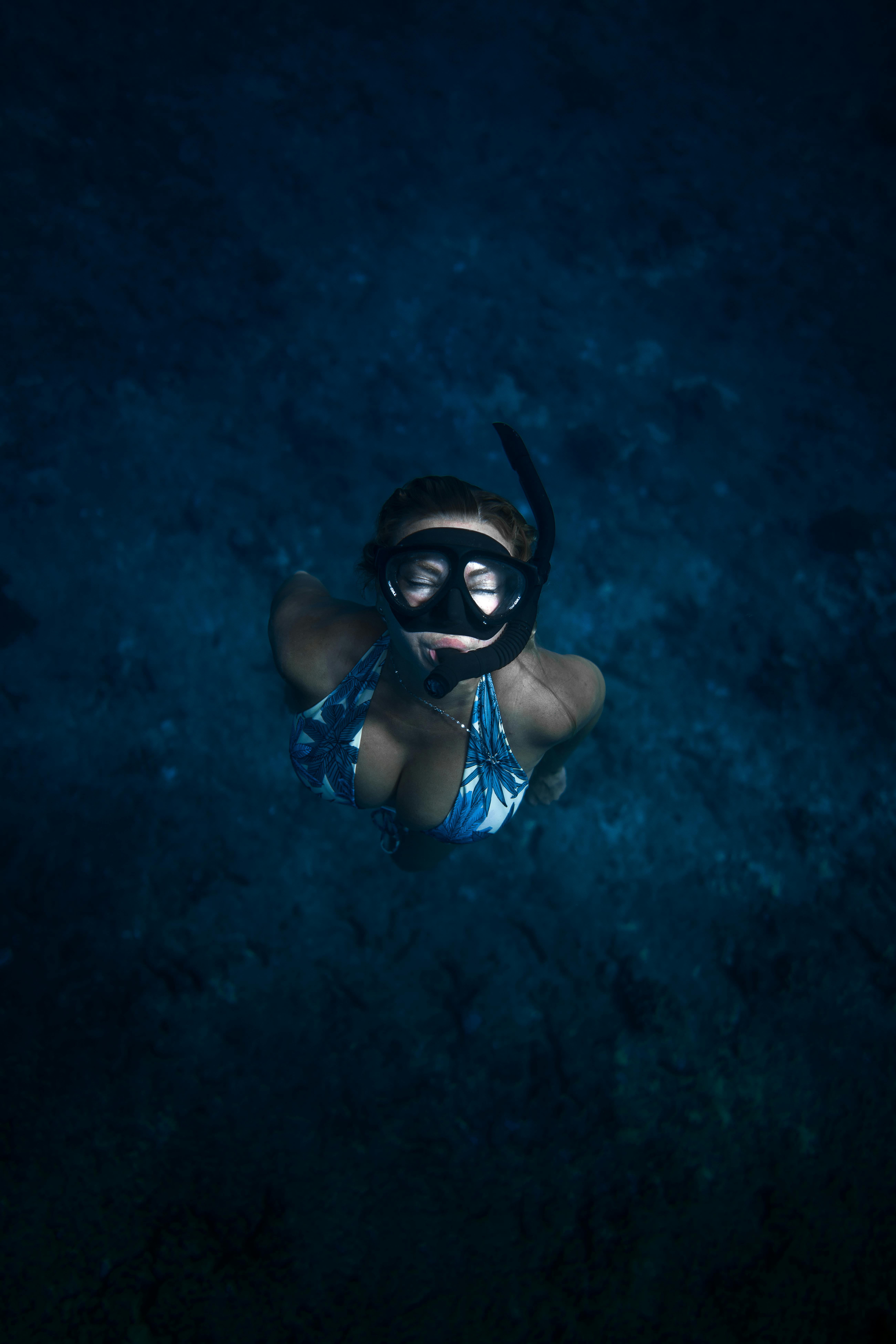 Top view slim female in swimwear and snorkel mask swimming with eyes closed deep in dark blue seawater