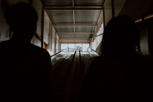 Free Two silhouettes stand on an indoor escalator in a dimly lit setting, offering a moody atmosphere. Stock Photo