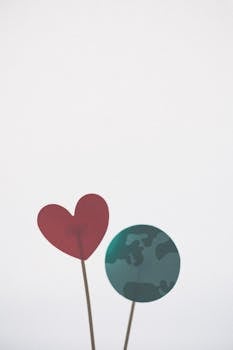 Minimalist display of Earth and heart shapes on sticks against a white background, emphasizing love and sustainability.
