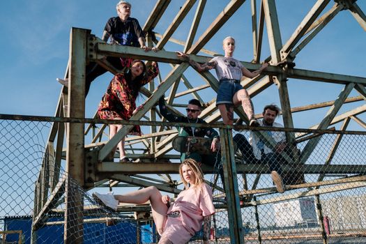 Young adults posing on an industrial structure in daylight, showcasing modern fashion and tattoos.