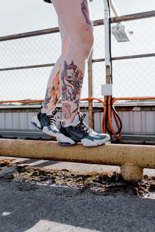 Free Person with colorful tattoos balancing on a rusty pipeline outdoors in sneakers. Stock Photo