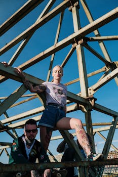 Two individuals in a punk style pose on an industrial structure under a clear blue sky.