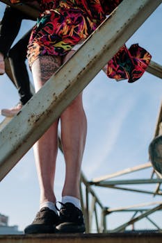 Vibrant tattooed legs in colorful shorts standing on an industrial metal structure.