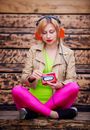 Focused female wearing colorful outfit and headphones sitting on stairway with crossed legs while listening to music and changing cassette in portable tape player