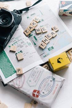 Flat lay of scrabble tiles spelling 'Take Me There' on a map with a camera, ideal for travel concept.