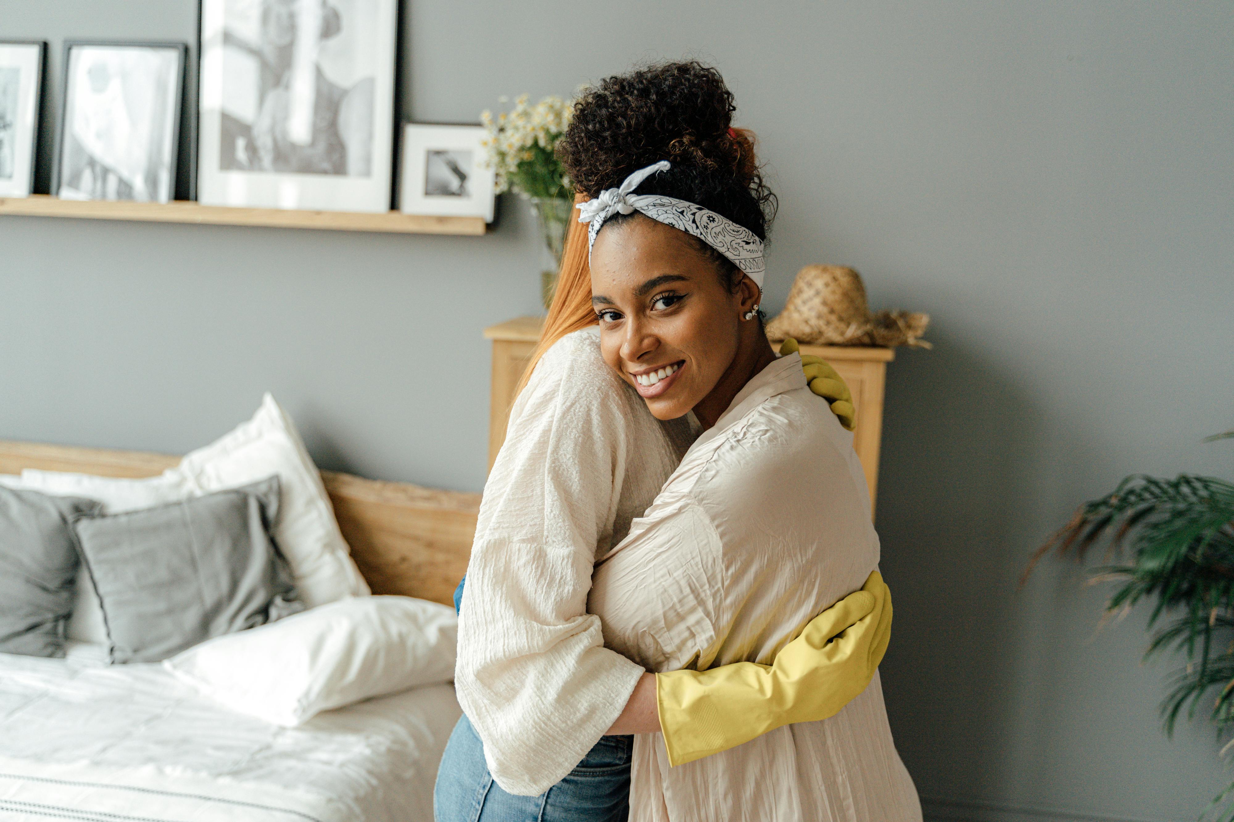 woman in white long sleeve shirt and blue denim jeans hugging woman in yellow long sleeve