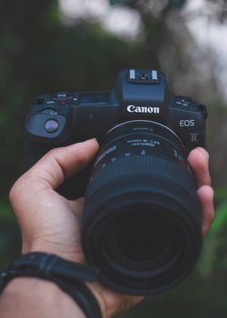 A close-up image of hands holding a DSLR camera outdoors, showcasing photography equipment.