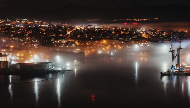 城市港口的空中夜景，充满活力的光和反射的雾，展示了城市和工业风景