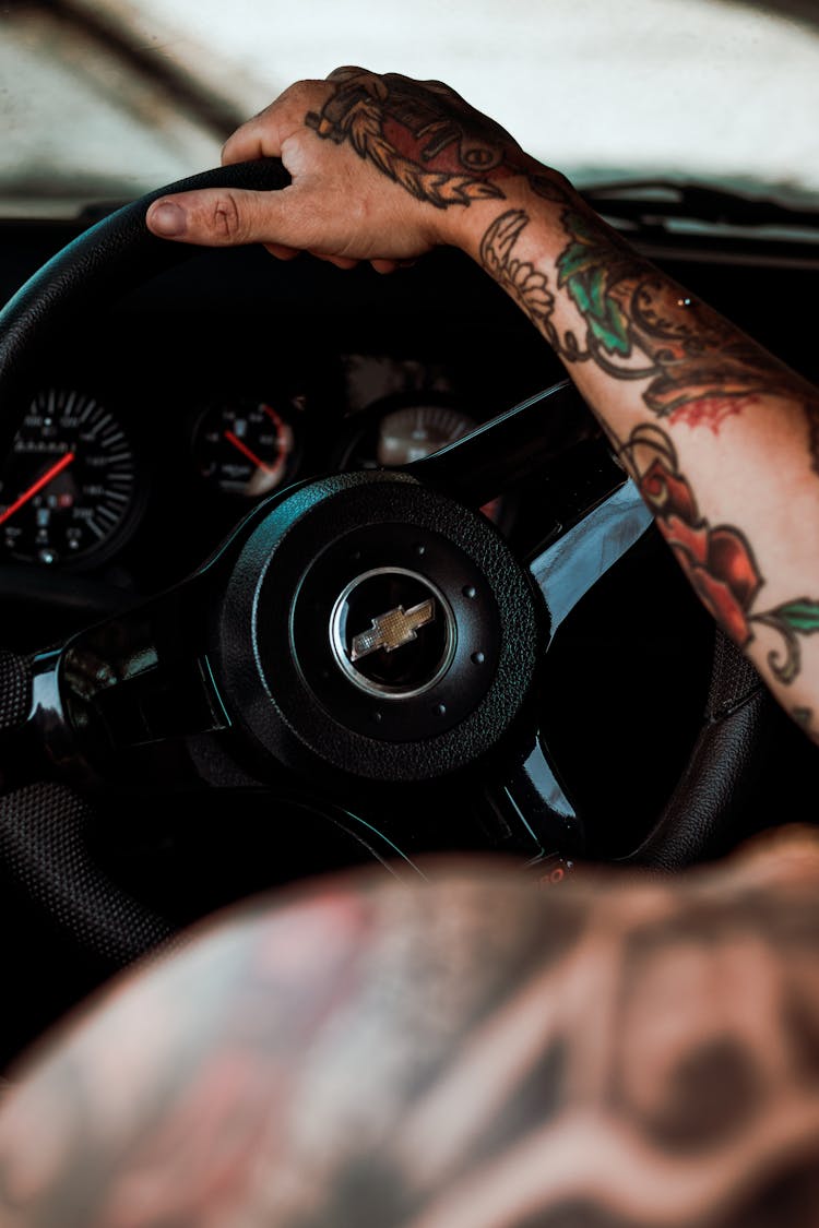 A Tattooed Person Driving A Car