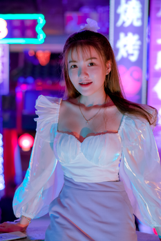 Happy young Asian female millennial in trendy outfit resting on modern city street with bright neon illumination at night and looking at camera