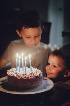 Two boys enjoying a birthday celebration with a cake featuring lit candles.