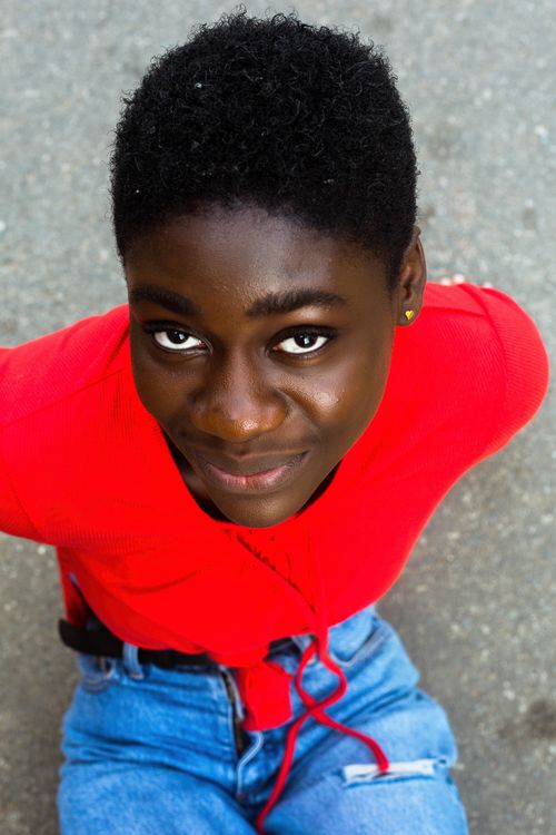 Free A cheerful individual looks up while sitting outdoors in a vibrant red shirt. Stock Photo