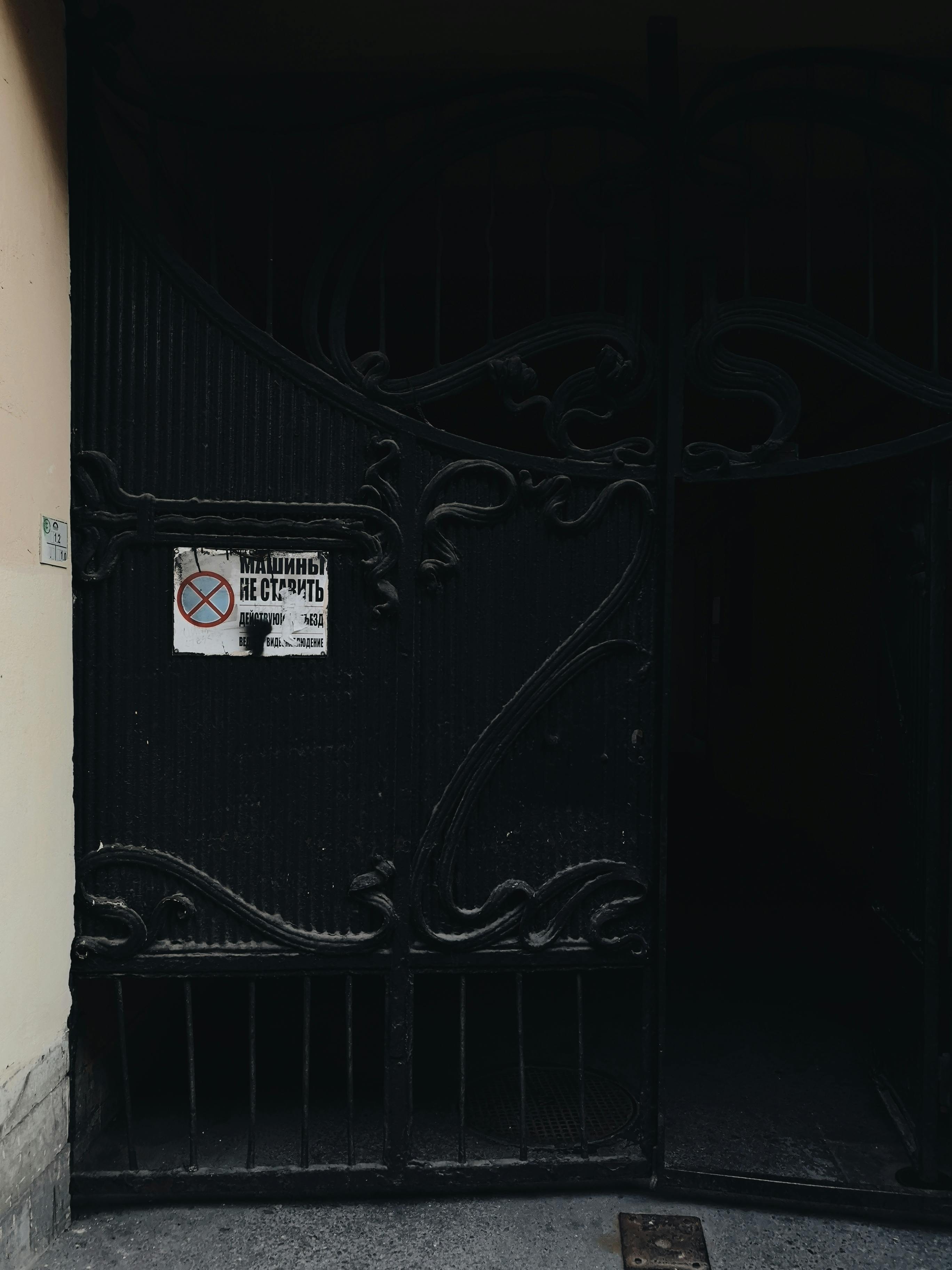 Close-up of a decorative metal gate with a sign in a moody dark entrance. Urban architectural detail.