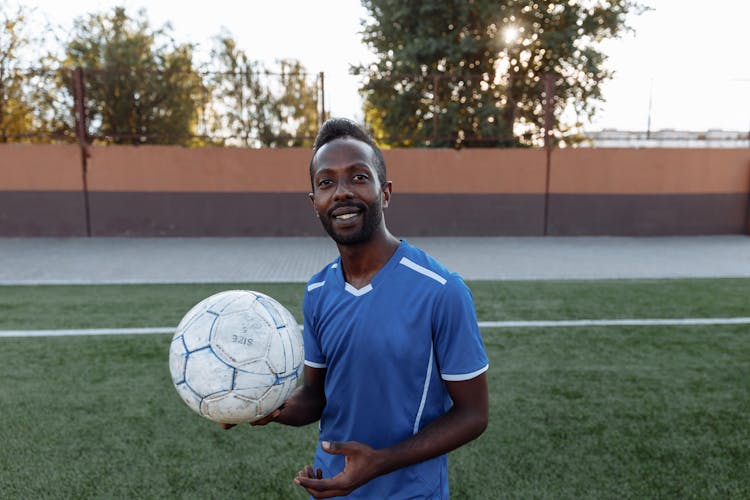 Man In Blue Shirt Holding Soccer Ball Smiling 