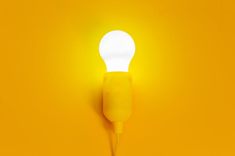 White Light Bulb Turned On In Yellow Background 