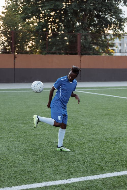 Free A young male soccer player in blue jersey practicing on a grass field during the day. Stock Photo